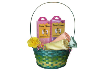 Green woven Easter basket with handle holding two Morning Glamour satin pillowcases in pink packaging, plus rolled pastel satin pillowcases in yellow, peach, and mint, accented with a yellow flower and colorful paper grass.